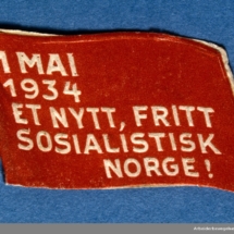 Arbeiderpartiets 1. mai-merke fra 1934 (OBS! er ikke i samlingen) men ligger i Arbeiderbevegelsen arkiv Bilde tilhører digitalt museum